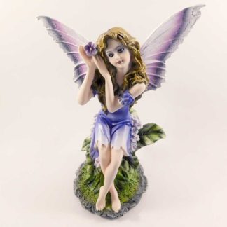 The fairy sits on a green, leafy seat with her legs crossed. She's cupping a purple flower over her ear