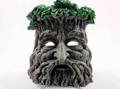 The front view - a mans face created with branches, his hair green leaves, his eyes are hollow to see the candle flickering in the back