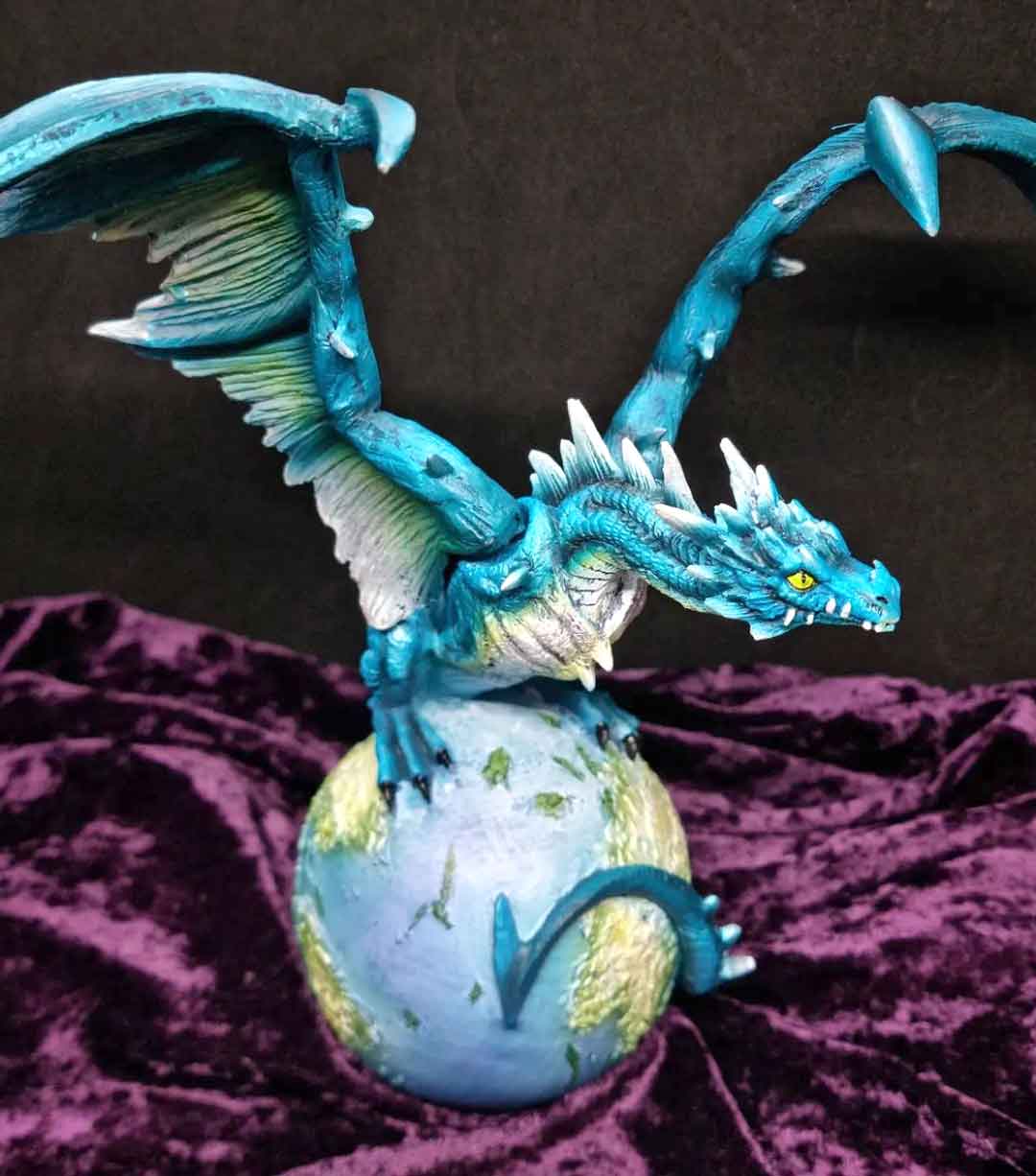 A blue dragon, wings outstretched, sitting on a globe of the world