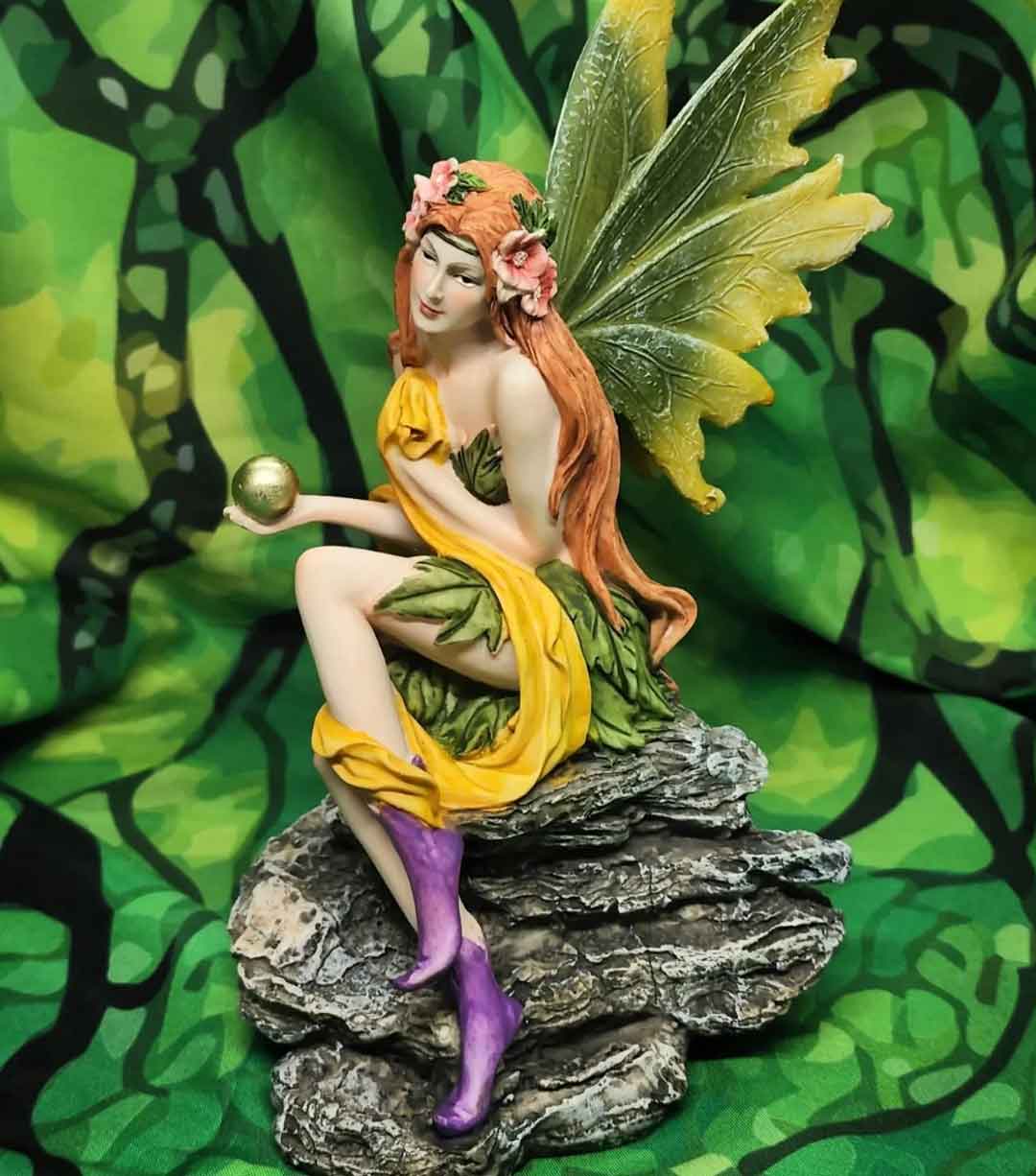 Red haired fairy with a green dress and green butterfly wings sitting on a rock